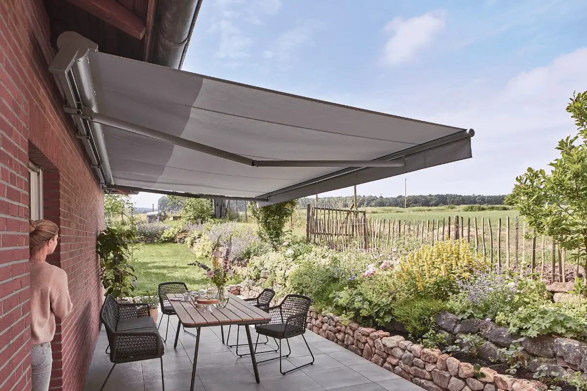Frau steht unter einer ausgefahrenen Markise auf einer Terrasse mit Gartenblick