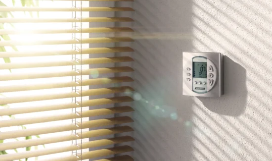 Sonnenlicht fällt durch Jalousien auf eine Wand mit einem digitalen Thermostat